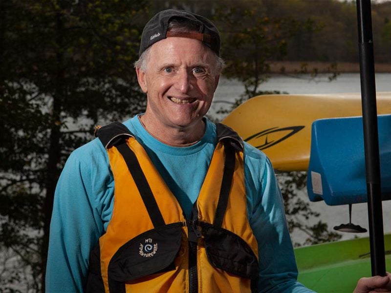 Man with a paddle in front of kayaks.