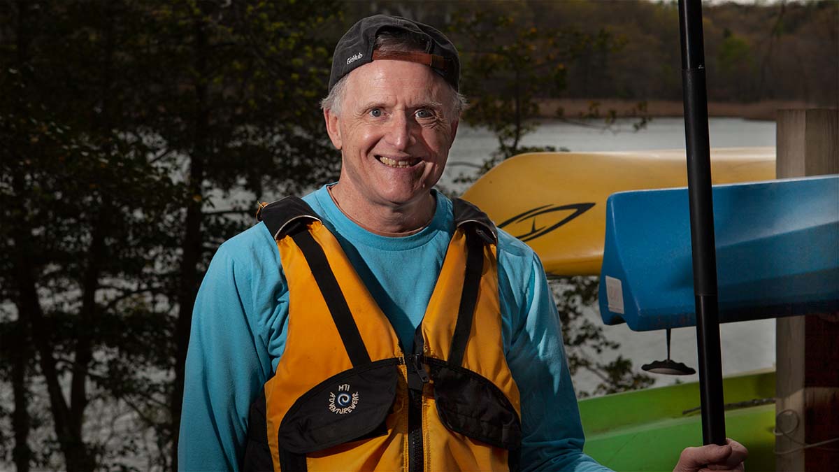 Man with a paddle in front of kayaks.